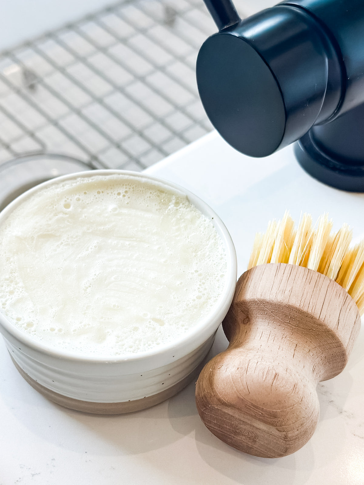 Bowl of soapy water with a wooden brush on a white surface