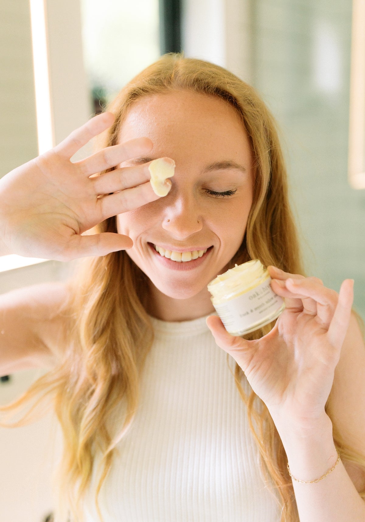 Woman applying cream to her face with a focus on skincare routine.