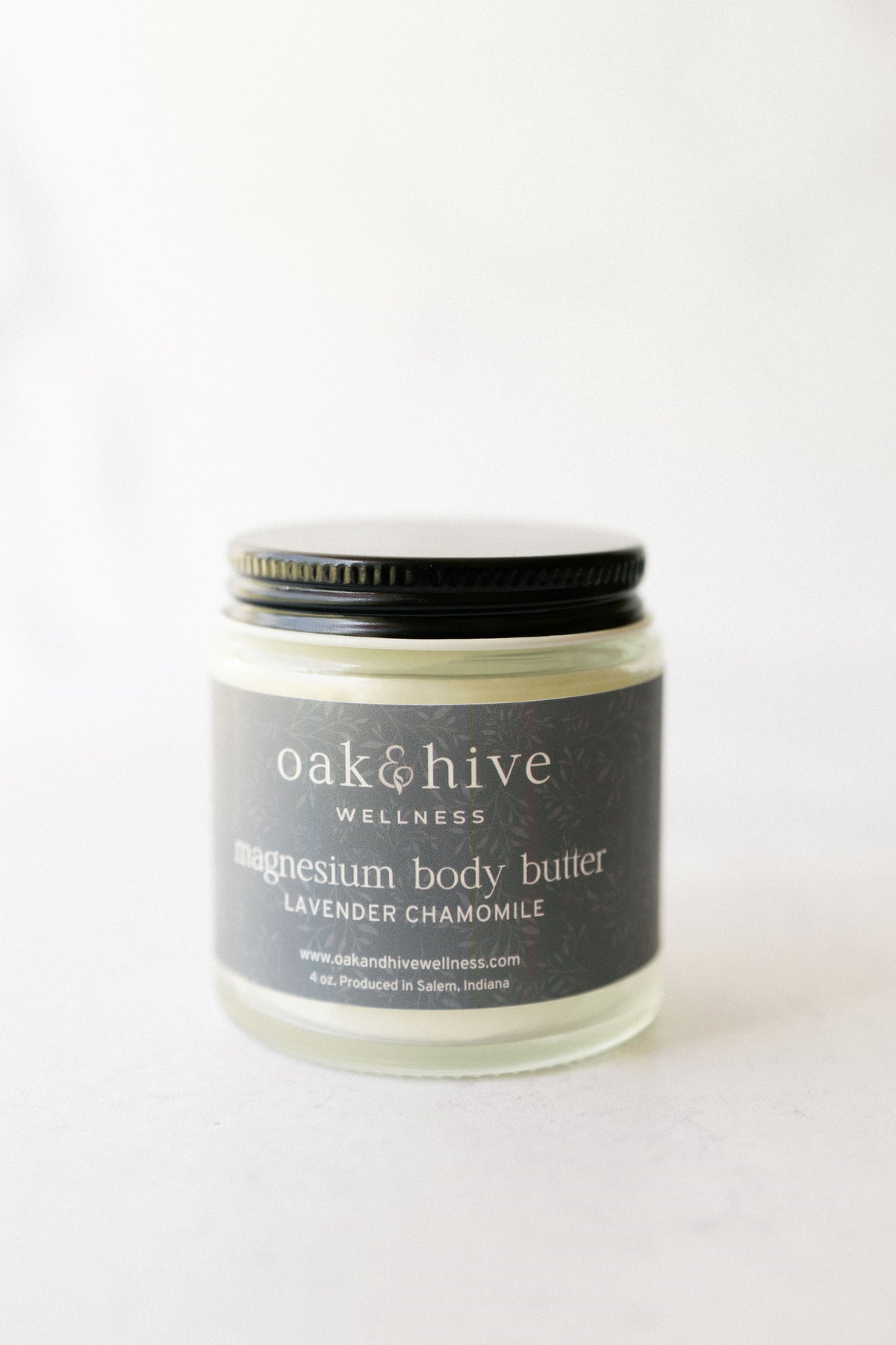 a jar of 'Oak & Hive Wellness Magnesium Body Butter, Lavender Chamomile' with a green label, a black lid on a white surface.