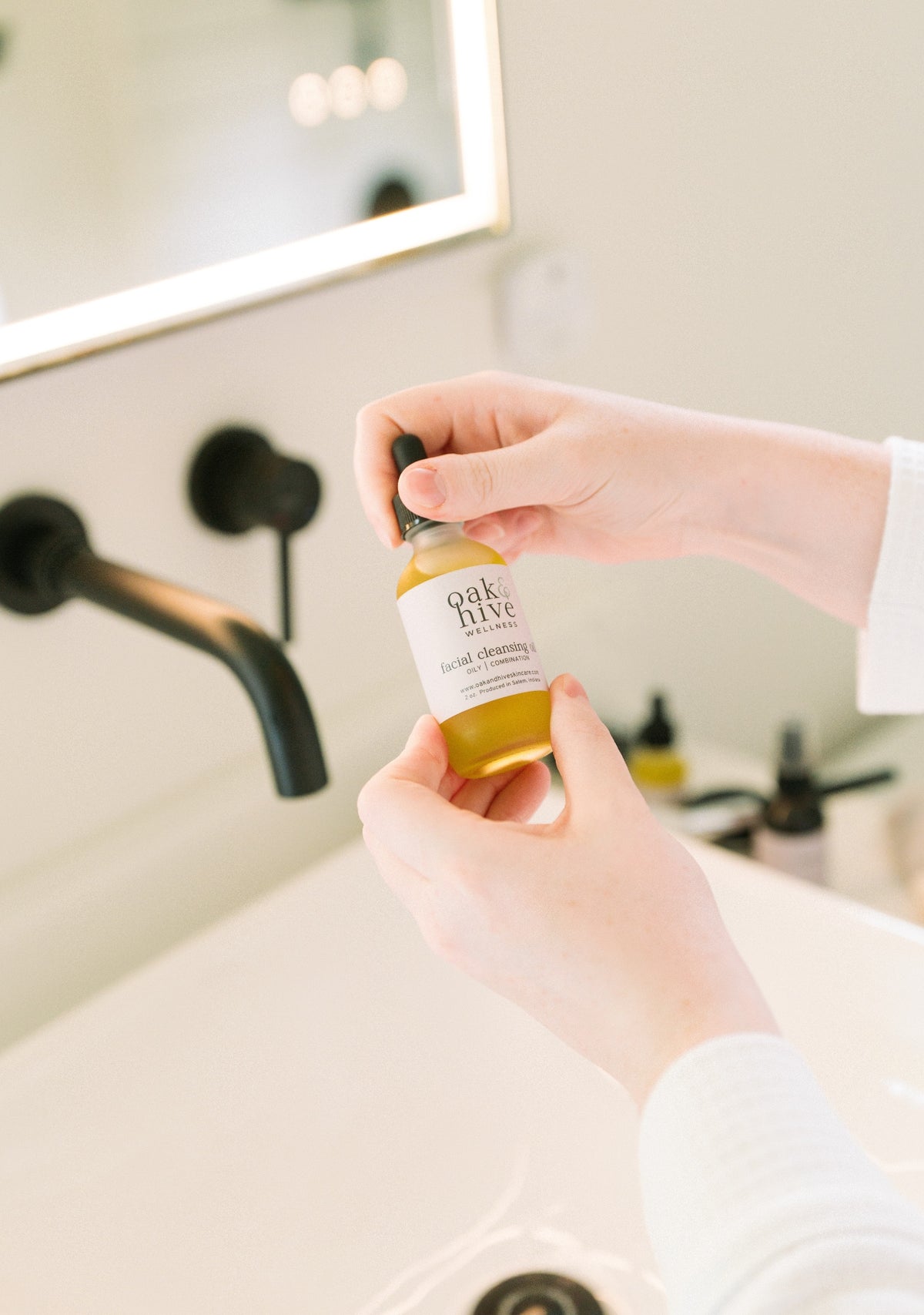 Person holding a bottle of 'Oak + Hive' product in a bathroom setting