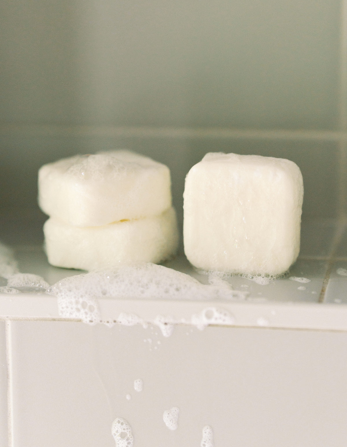 three bars of soap on a white surface with water droplets.