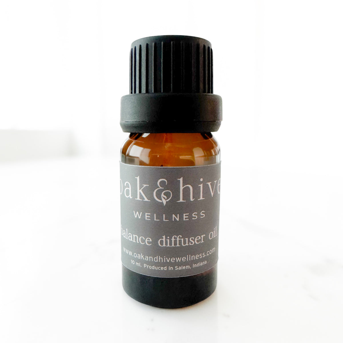 A small amber glass bottle of Oak & Hive Wellness balance diffuser oil with a black cap and dark gray label, photographed on a light white background.