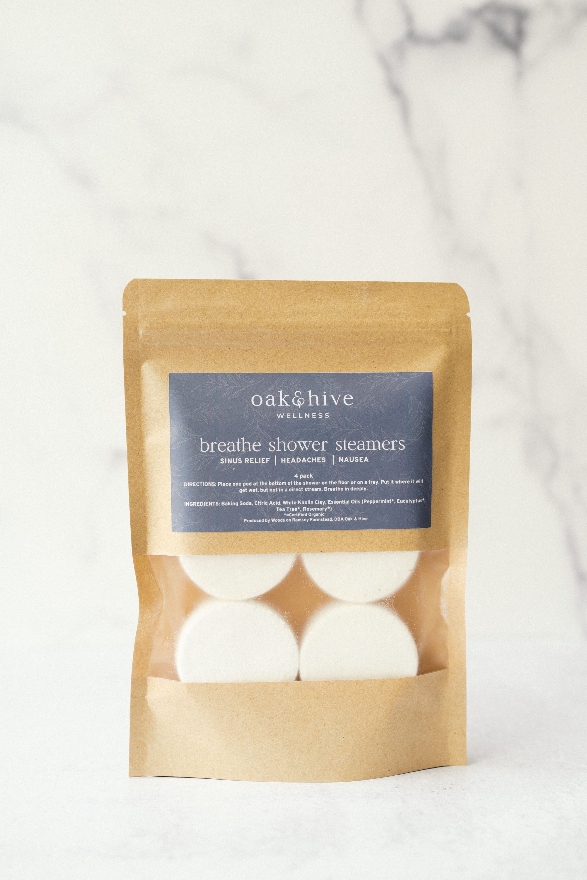 A package of Oak & Hive Shower Steamers with essential oils, placed on a marble surface. The package is labeled 'Breathe Shower Steamers' and contains several white tablets designed to dissolve in water for aromatherapy benefits.