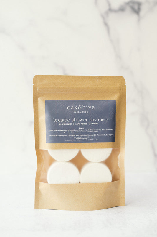 A package of Oak & Hive Shower Steamers with essential oils, placed on a marble surface. The package is labeled 'Breathe Shower Steamers' and contains several white tablets designed to dissolve in water for aromatherapy benefits.
