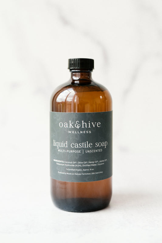 A brown bottle of Oak & Hive Liquid Castile Soap with a black cap and a green label that includes the product name and the brand's website.