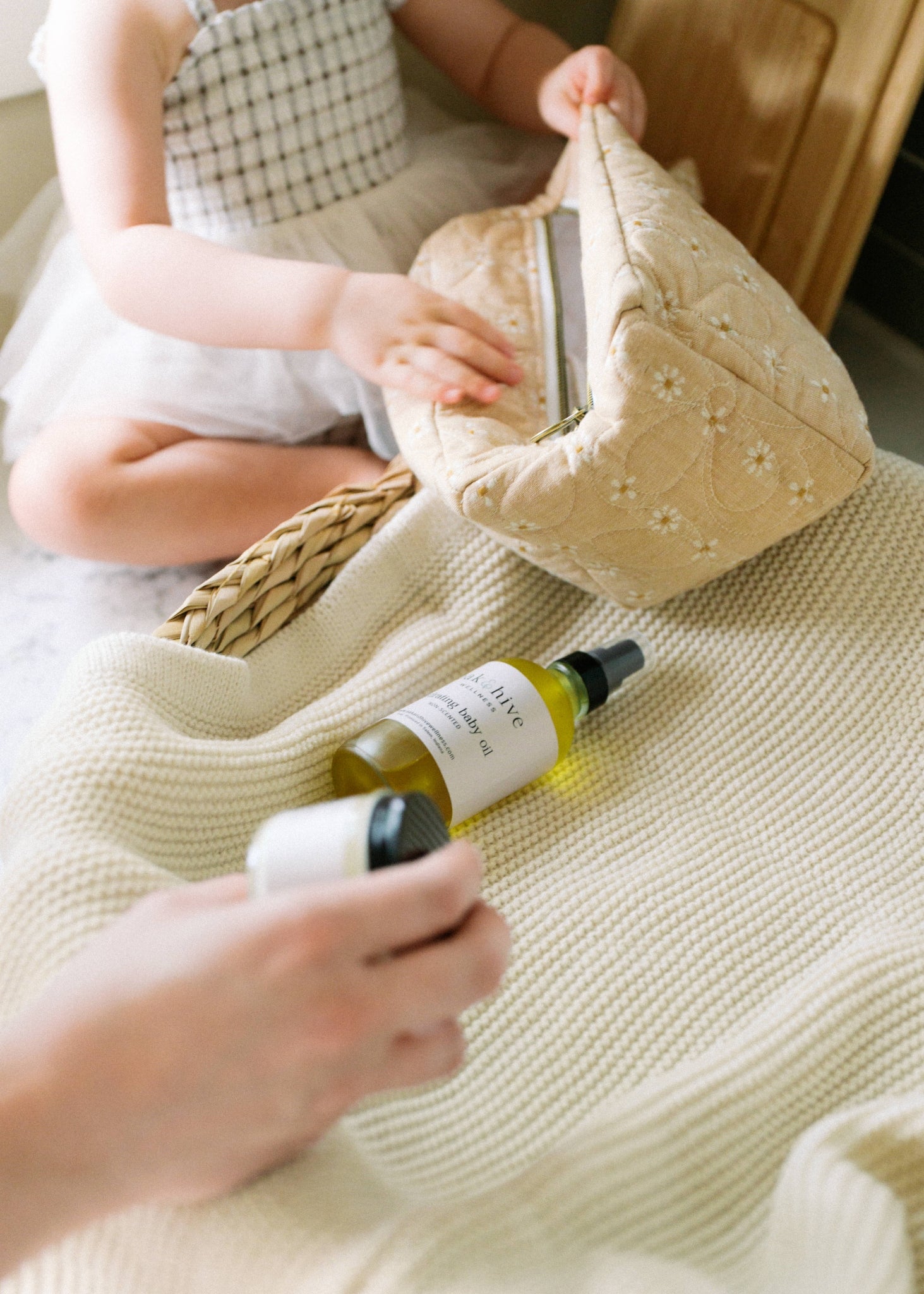  A young child and a mother removing a bottle of oil , and a jar from a yellow knit bag and laying the products on a cream colored surface. 