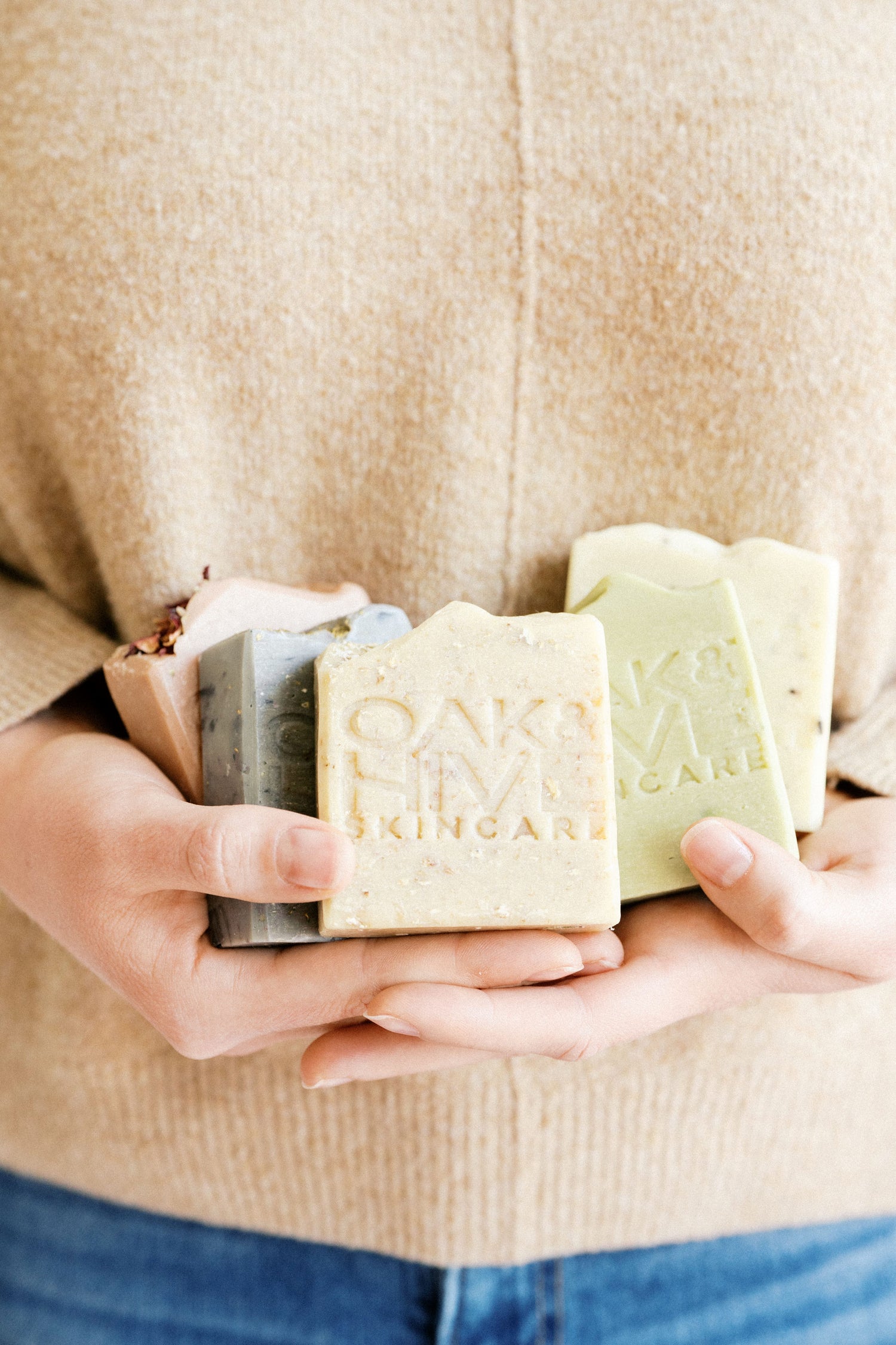 A person holding three bars of goat milk soap with various labels on them.