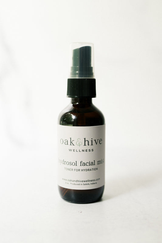 Black spray bottle labeled 'oak & hive wellness' rose hydrosol facial mist on a white background