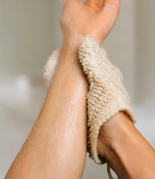 Close-up of a person wearing beige knitted sisal exfoliating glove with a neutral background
