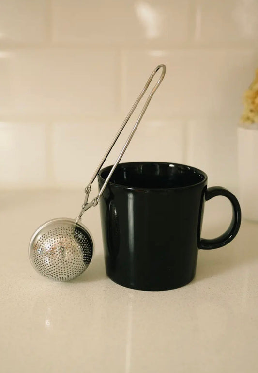 Black mug with a metal tea infuser on a light-colored surface