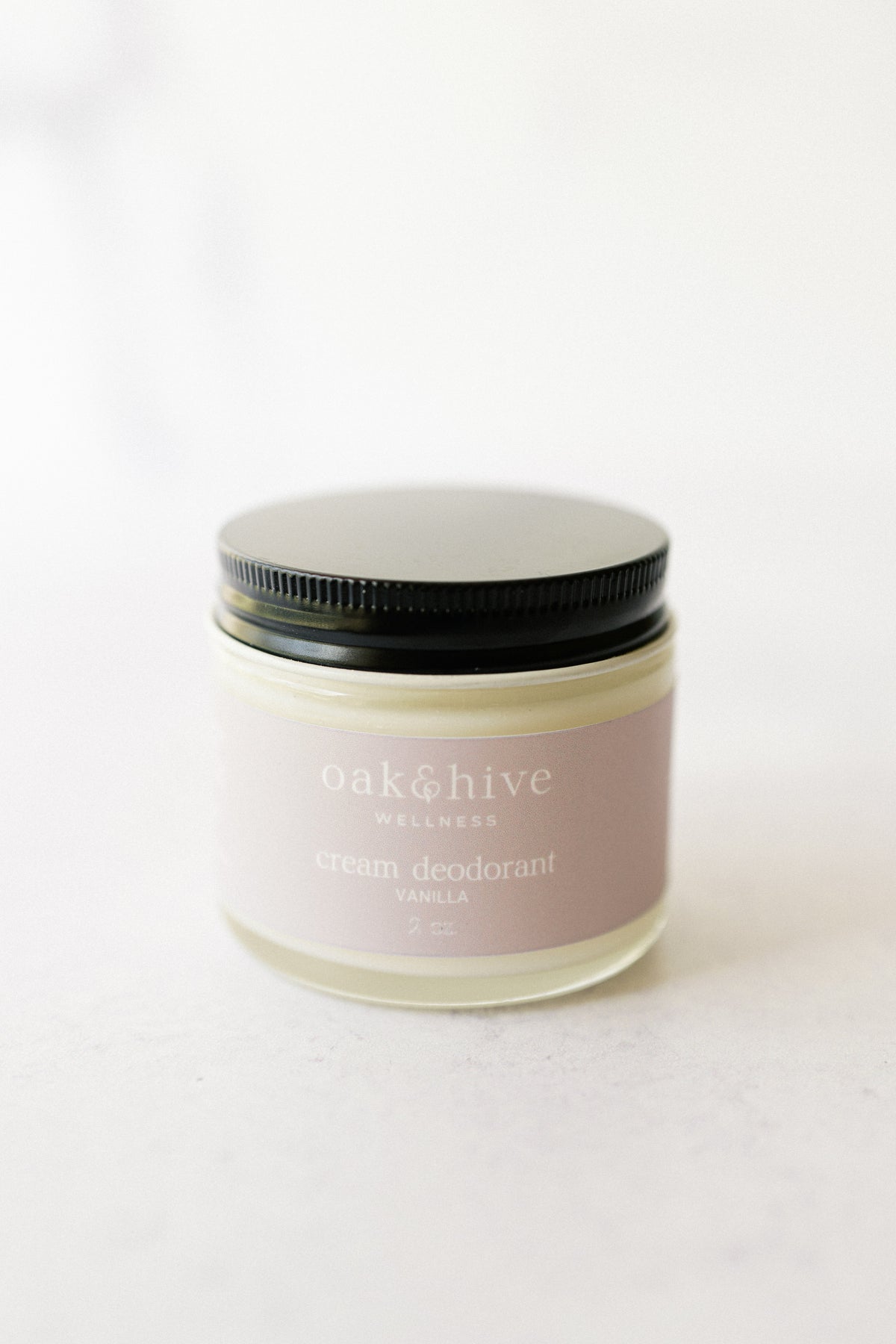 a jar of vanilla deodorant with a cream label, with a black lid on a white background. 